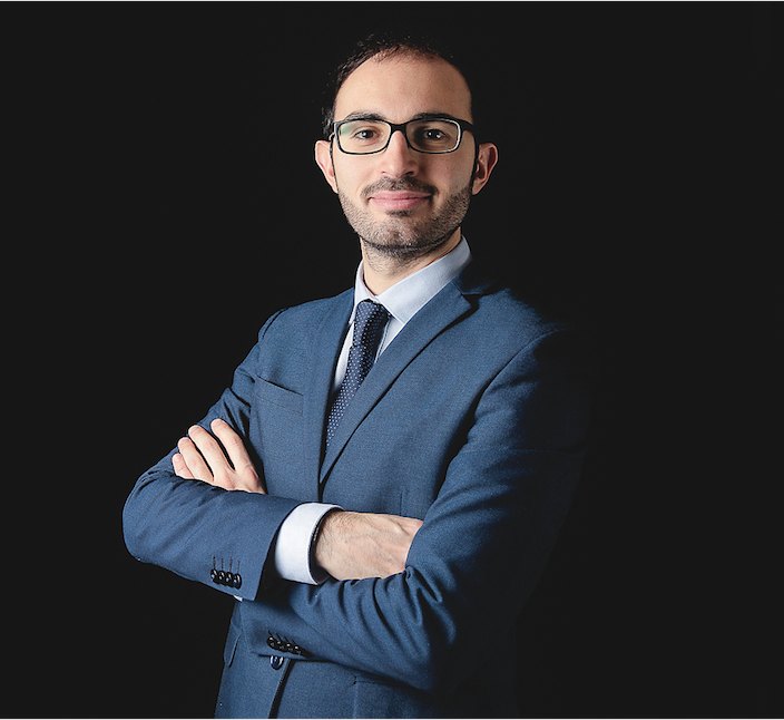 Davide Marino, ritratto a mezzo busto, giacca blu e occhiali, braccia conserte
